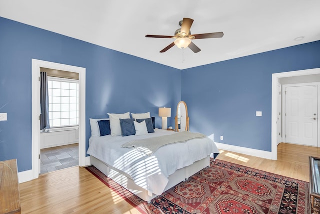 bedroom with wood finished floors, baseboards, ensuite bathroom, and a ceiling fan