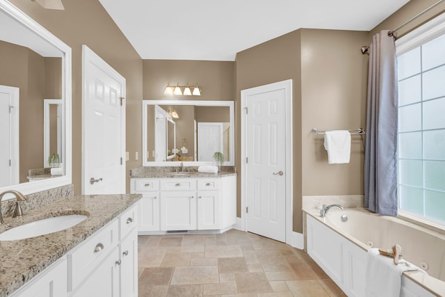full bathroom with a tub with jets, two vanities, stone finish floors, and baseboards