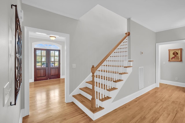 foyer entrance featuring crown molding, light wood-type flooring, stairway, french doors, and baseboards