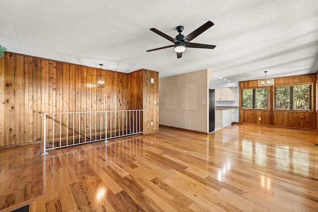 unfurnished room featuring ceiling fan with notable chandelier, a textured ceiling, light hardwood / wood-style floors, and wood walls