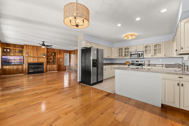 kitchen featuring light stone countertops, ceiling fan with notable chandelier, stainless steel appliances, pendant lighting, and light hardwood / wood-style floors