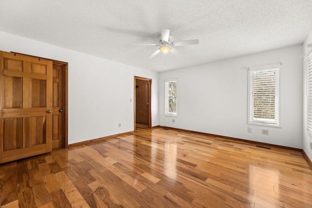 empty room with ceiling fan, light wood-type flooring, and a textured ceiling