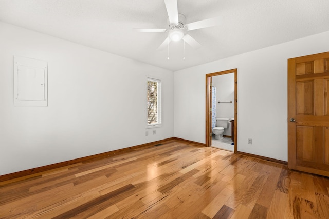 unfurnished bedroom featuring electric panel, light hardwood / wood-style floors, ensuite bath, and ceiling fan