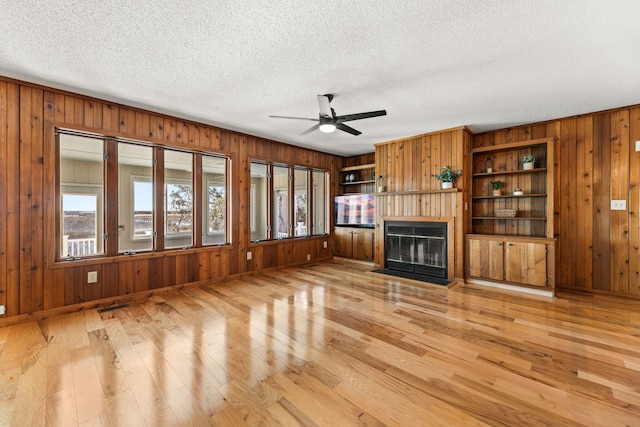 unfurnished living room with ceiling fan, wooden walls, and light hardwood / wood-style flooring