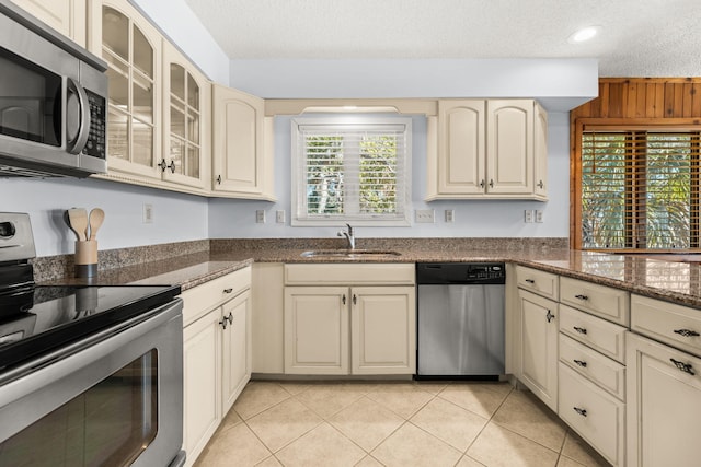 kitchen with a textured ceiling, cream cabinetry, sink, and appliances with stainless steel finishes