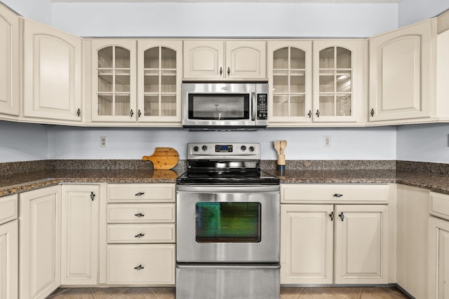 kitchen with cream cabinets, dark stone counters, and appliances with stainless steel finishes