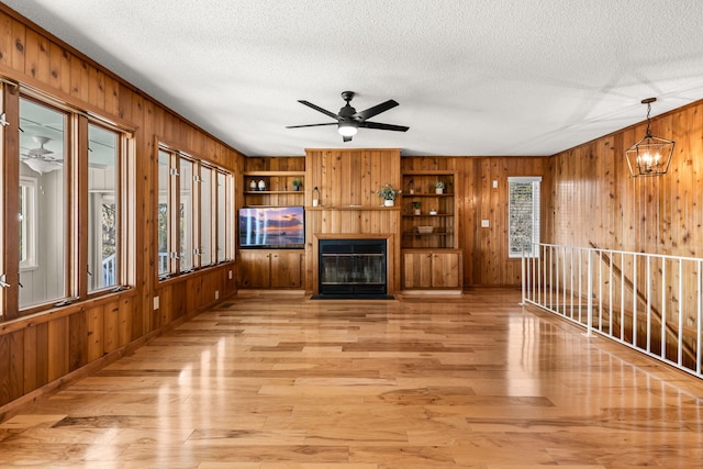 unfurnished living room featuring ceiling fan with notable chandelier, light wood-type flooring, and a healthy amount of sunlight