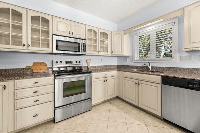 kitchen featuring cream cabinets, sink, a textured ceiling, appliances with stainless steel finishes, and light tile patterned flooring