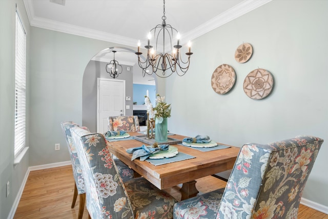 dining area featuring arched walkways, a notable chandelier, light wood-style flooring, and ornamental molding