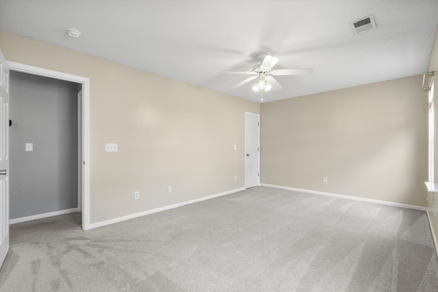 carpeted empty room featuring visible vents, a ceiling fan, and baseboards