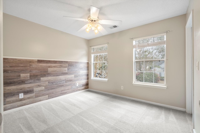 empty room with ceiling fan, visible vents, carpet floors, and wood walls