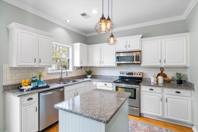 kitchen with visible vents, a sink, hanging light fixtures, stainless steel appliances, and white cabinetry