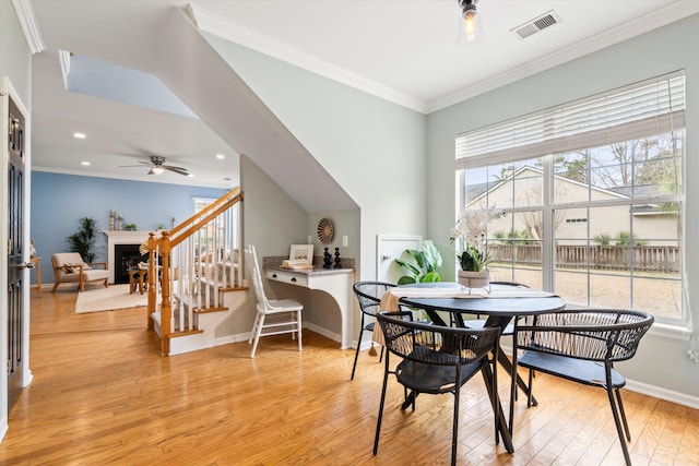 dining room featuring visible vents, light wood finished floors, a fireplace, crown molding, and baseboards