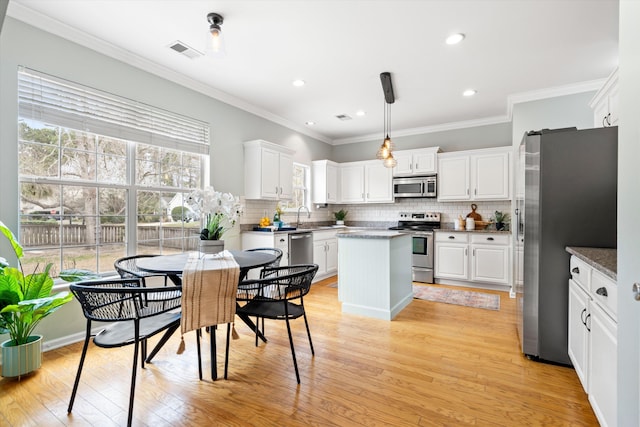 kitchen with light wood-style flooring, a center island, white cabinetry, appliances with stainless steel finishes, and decorative backsplash