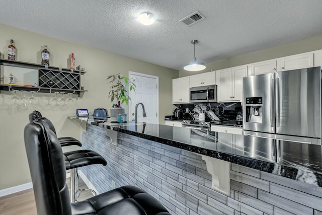 kitchen featuring hanging light fixtures, appliances with stainless steel finishes, a textured ceiling, white cabinets, and dark stone counters