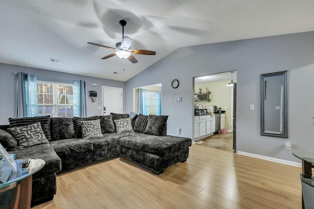 living room with lofted ceiling, light wood-type flooring, a textured ceiling, and ceiling fan