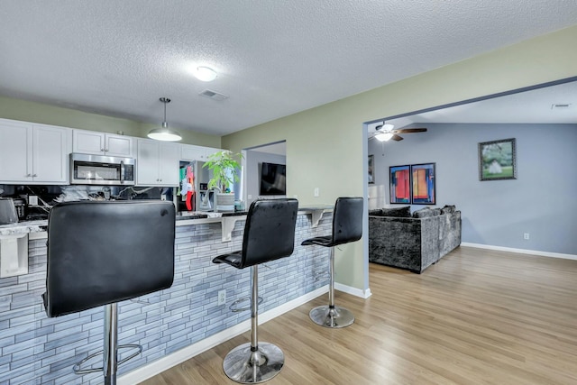 kitchen with decorative light fixtures, decorative backsplash, light hardwood / wood-style flooring, a textured ceiling, and white cabinets