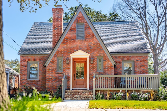 tudor house with brick siding, a chimney, and a shingled roof