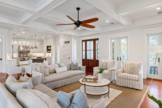 living room with coffered ceiling, wooden walls, ceiling fan, light hardwood / wood-style floors, and beam ceiling