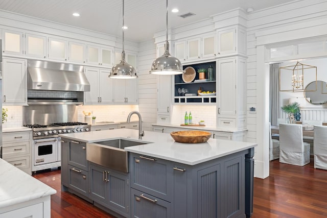 kitchen featuring pendant lighting, luxury stove, a center island with sink, sink, and white cabinetry