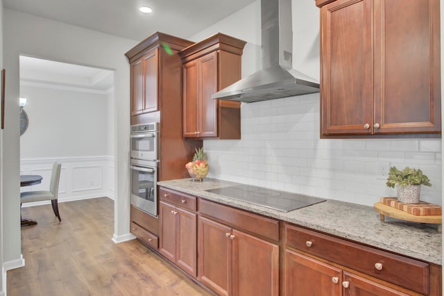 kitchen with light stone countertops, black electric stovetop, light wood-type flooring, and wall chimney exhaust hood