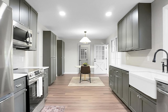 kitchen featuring gray cabinets, appliances with stainless steel finishes, decorative light fixtures, sink, and light hardwood / wood-style floors