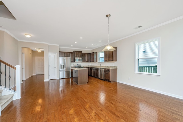 kitchen with a center island, ornamental molding, appliances with stainless steel finishes, and wood-type flooring