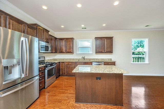 kitchen featuring sink, ornamental molding, appliances with stainless steel finishes, wood-type flooring, and light stone counters