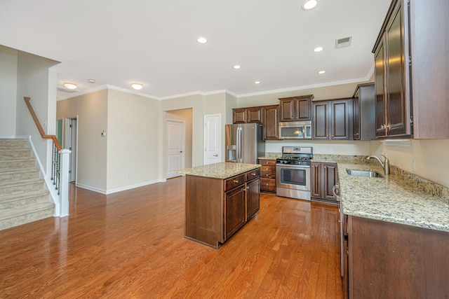 kitchen featuring stainless steel appliances, sink, light stone counters, wood-type flooring, and a center island