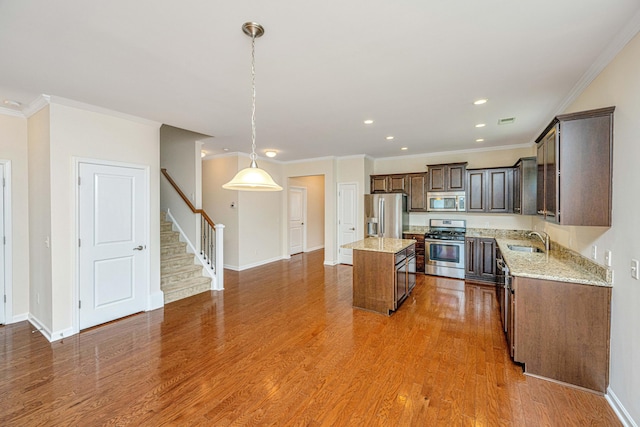 kitchen with appliances with stainless steel finishes, hardwood / wood-style floors, sink, light stone countertops, and a kitchen island