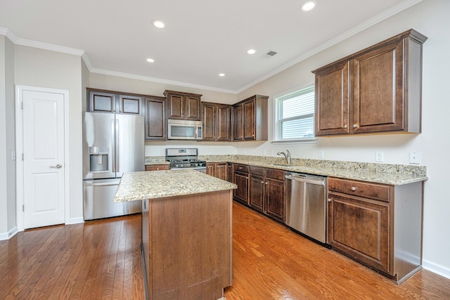 kitchen with ornamental molding, dark brown cabinetry, wood-type flooring, a kitchen island, and stainless steel appliances