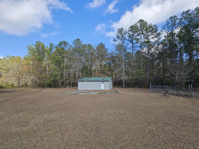 view of yard with fence, a storage unit, a forest view, and an outbuilding