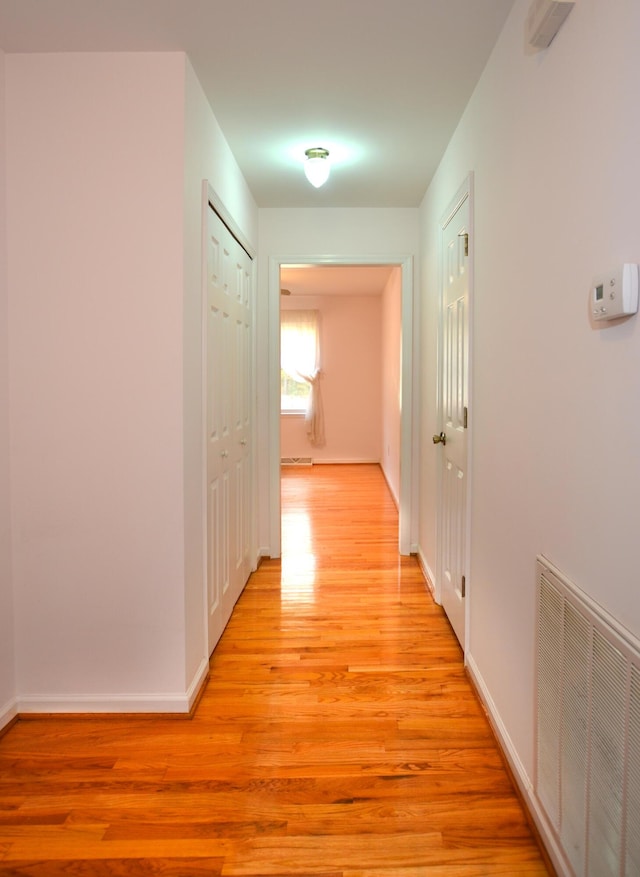 hall featuring baseboards, visible vents, and light wood finished floors