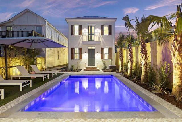 back of property at dusk featuring a standing seam roof, a balcony, a fenced backyard, and metal roof