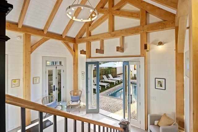 doorway to outside with beamed ceiling, an inviting chandelier, high vaulted ceiling, and wooden walls