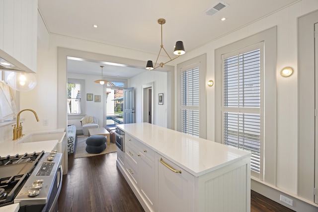 kitchen with visible vents, dark wood-type flooring, a sink, white cabinets, and stainless steel gas range