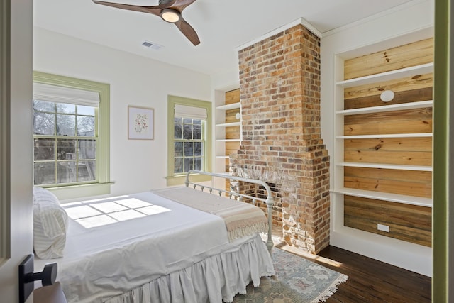 bedroom with dark wood-style floors, visible vents, a fireplace, and ceiling fan