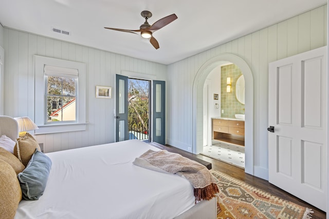 bedroom with wood finished floors, visible vents, arched walkways, access to exterior, and connected bathroom