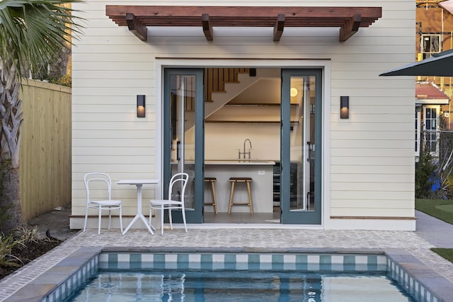 back of property featuring a sink, an outdoor pool, a patio, and fence