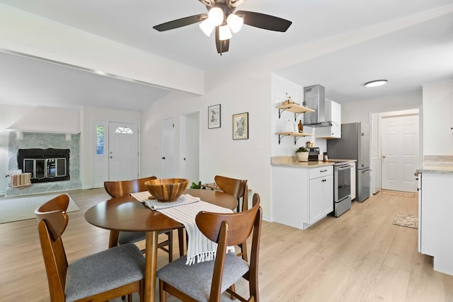 dining space with light wood finished floors, a premium fireplace, and a ceiling fan