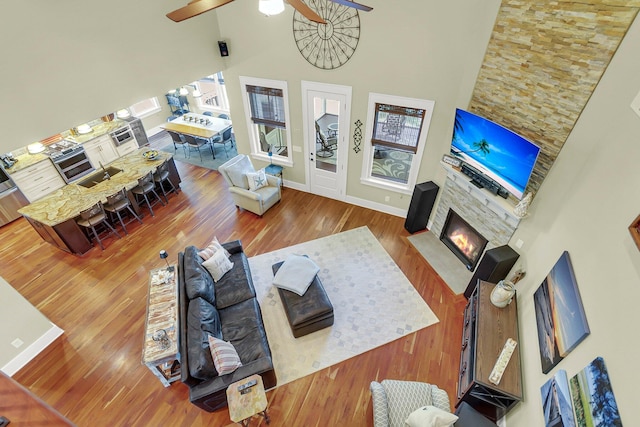 living room with hardwood / wood-style floors, a high ceiling, a fireplace, and ceiling fan