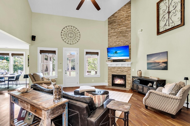 living room with hardwood / wood-style flooring, a stone fireplace, plenty of natural light, and high vaulted ceiling