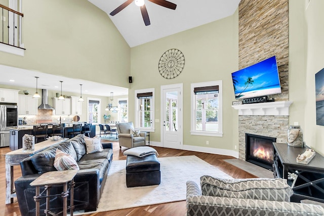 living room with hardwood / wood-style flooring, high vaulted ceiling, a healthy amount of sunlight, and a stone fireplace