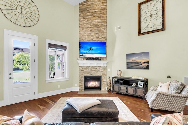 living room featuring hardwood / wood-style floors, a high ceiling, and a stone fireplace