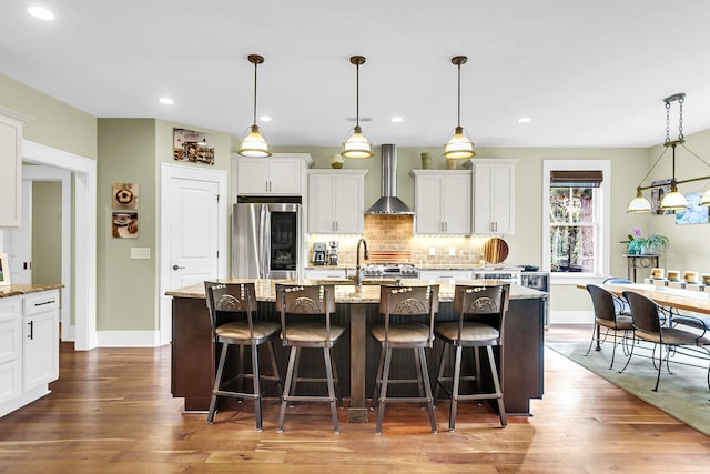 kitchen with pendant lighting, appliances with stainless steel finishes, a center island with sink, and wall chimney range hood