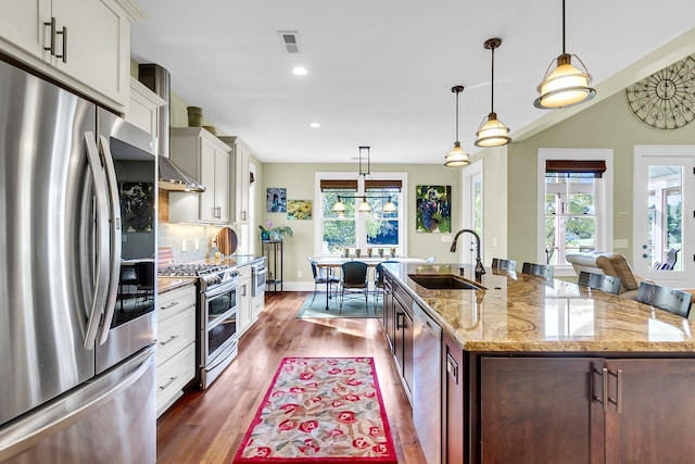 kitchen featuring stainless steel appliances, dark hardwood / wood-style flooring, a center island with sink, hanging light fixtures, and sink