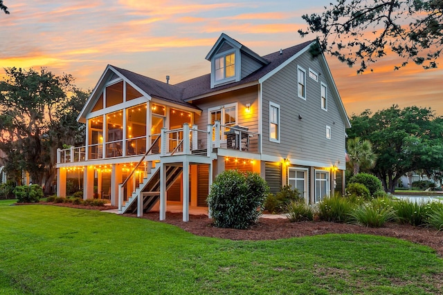 back house at dusk featuring a lawn and a sunroom