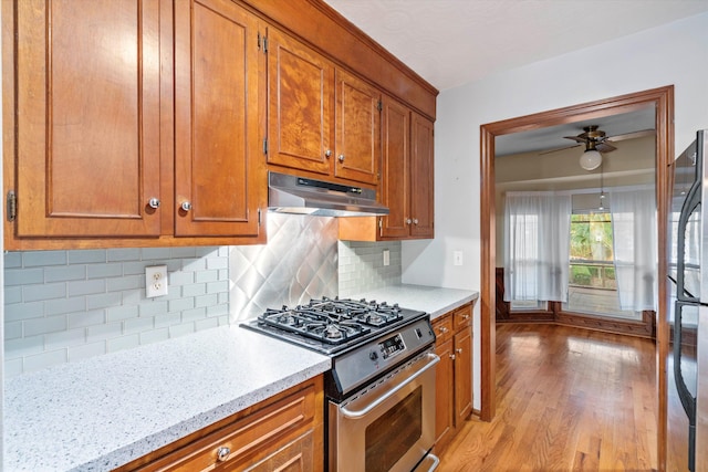 kitchen featuring stainless steel gas range oven, light wood finished floors, under cabinet range hood, freestanding refrigerator, and brown cabinetry