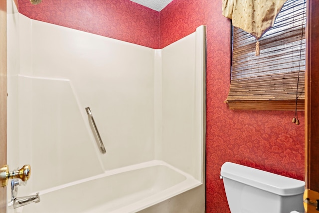 bathroom with wallpapered walls,  shower combination, and toilet