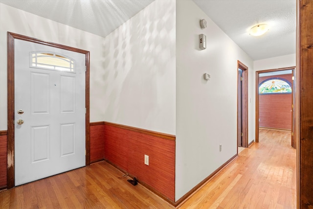 entrance foyer featuring wooden walls, wainscoting, a textured ceiling, and light wood-style flooring